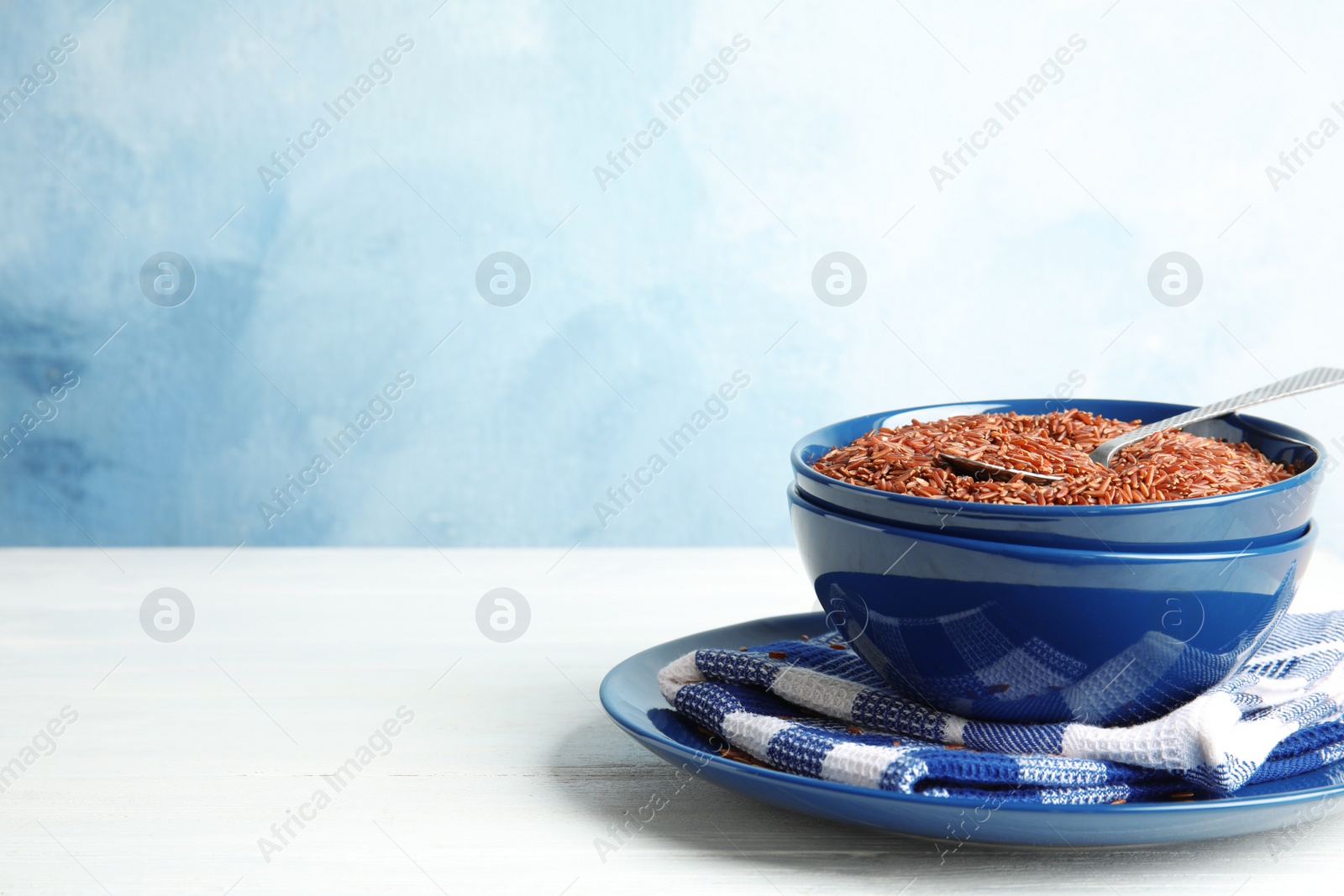 Photo of Bowl with uncooked red rice on white table. Space for text