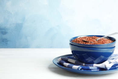 Photo of Bowl with uncooked red rice on white table. Space for text