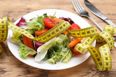 Photo of Plate with fresh vegetable salad and measuring tape on wooden table. Healthy diet concept