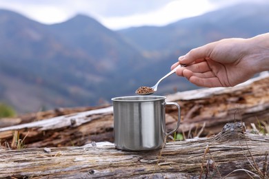 Photo of Woman pouring instant coffee into mug in mountains, closeup