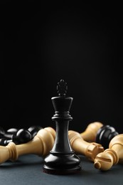 Photo of Black king among fallen chess pieces on dark background. Space for text