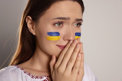 Sad young Ukrainian woman with clasped hands on beige background, closeup