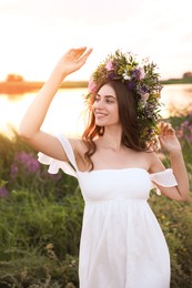 Photo of Young woman wearing wreath made of beautiful flowers outdoors