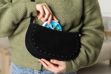 Photo of Woman putting pill box into bag indoors, closeup