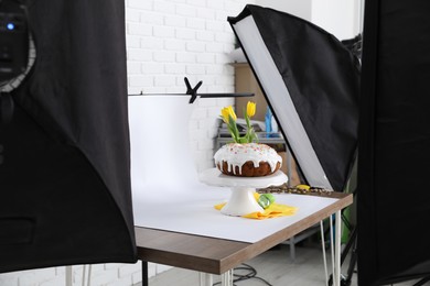 Photo of Professional equipment and composition with delicious Easter cake on wooden table in studio. Food photography