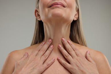 Photo of Mature woman touching her neck on grey background, closeup