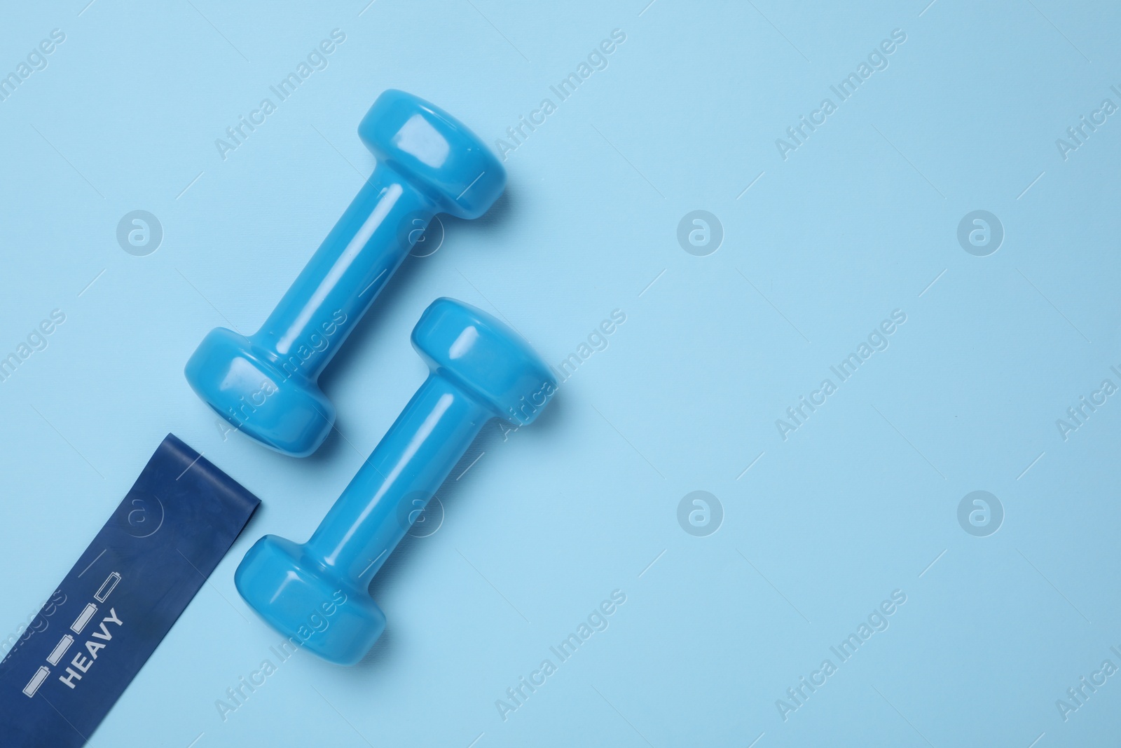 Photo of Two dumbbells and fitness elastic band on light blue background, flat lay. Space for text