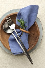 Photo of Stylish setting with cutlery, napkin, rosemary and plates on light textured table, top view