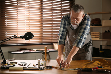 Man cutting leather with knife in workshop