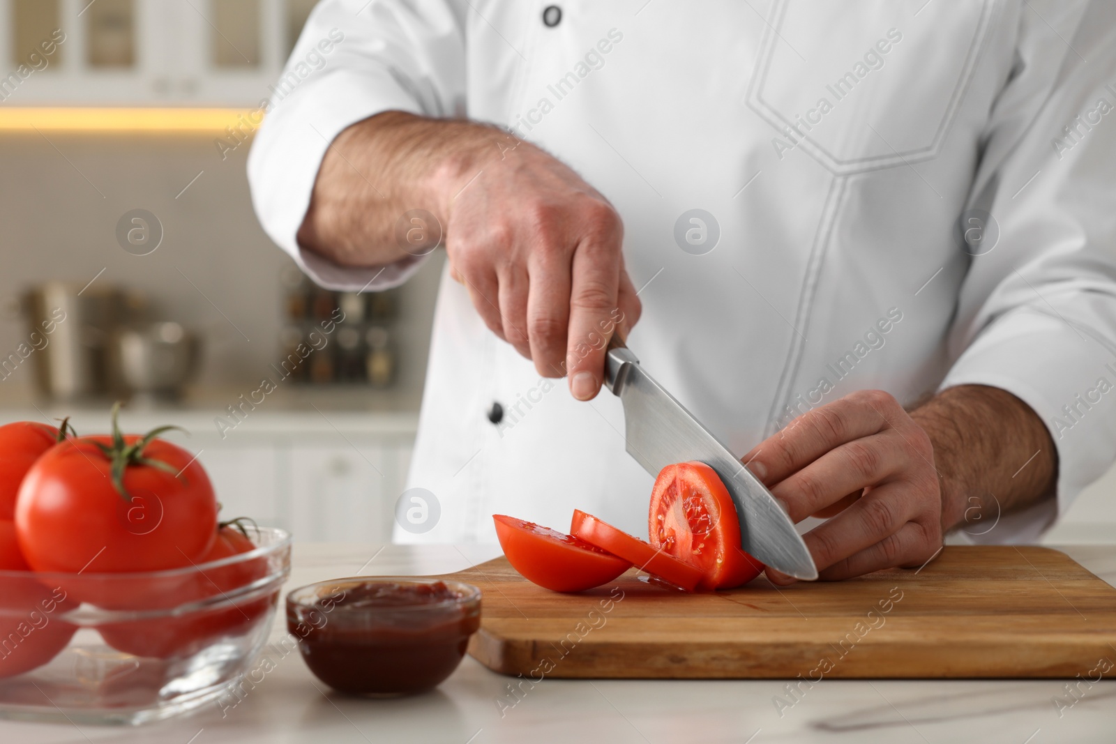 Photo of Professional chef cutting tomatoes at white marble table indoors, closeup