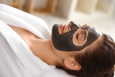 Beautiful woman with black mask on face relaxing in spa salon