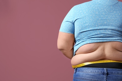 Overweight woman with measuring tape on color background