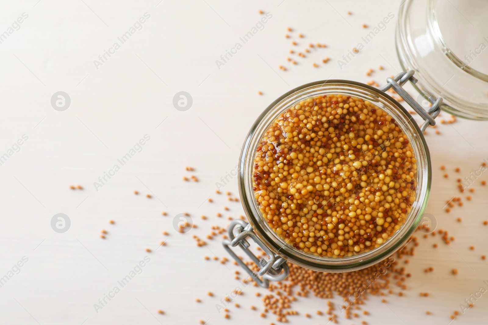 Photo of Jar of whole grain mustard on white wooden table, top view. Space for text