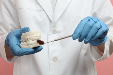 Doctor holding dental model with jaws and tool on pink background, closeup. Cast of teeth