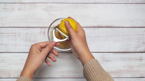 Photo of Man peeling lemon at white wooden table, top view