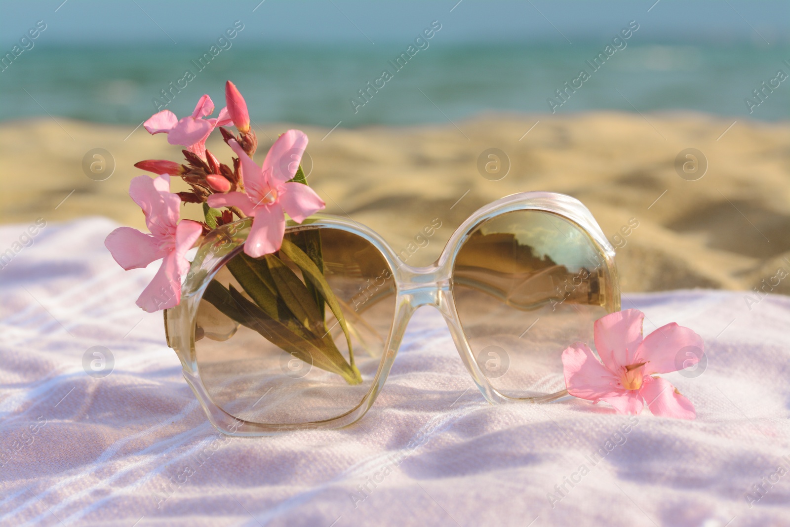 Photo of Beautiful sunglasses with tropical flower on blanket near sea, closeup