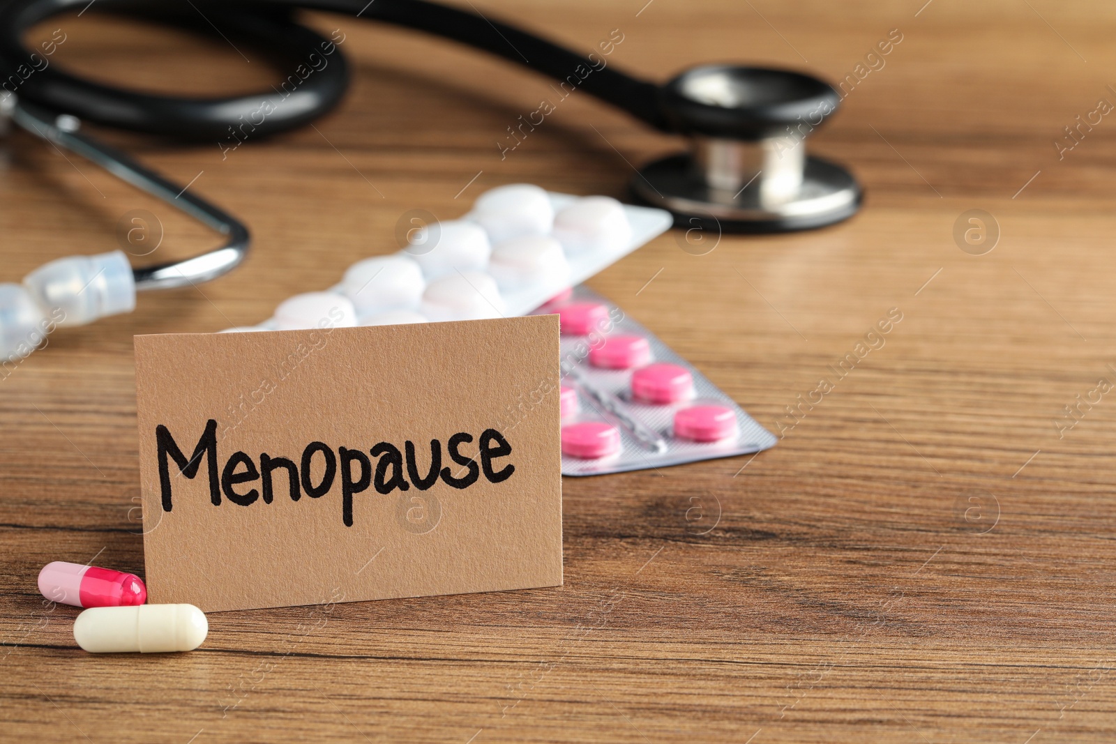 Photo of Card with word Menopause, pills and stethoscope on wooden table, space for text