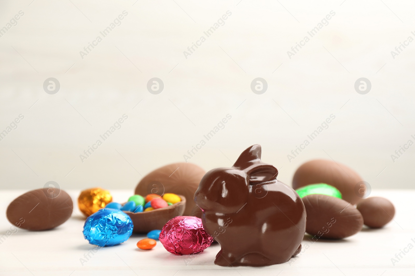 Photo of Chocolate Easter bunny and eggs on white table. Space for text