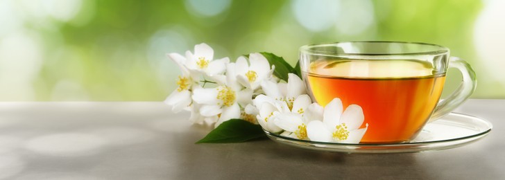 Cup of jasmine tea and fresh flowers on grey table outdoors, space for text. Banner design