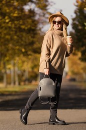 Photo of Young woman with stylish backpack and hot drink on autumn day