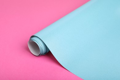 Photo of Roll of light blue wrapping paper on pink background, closeup