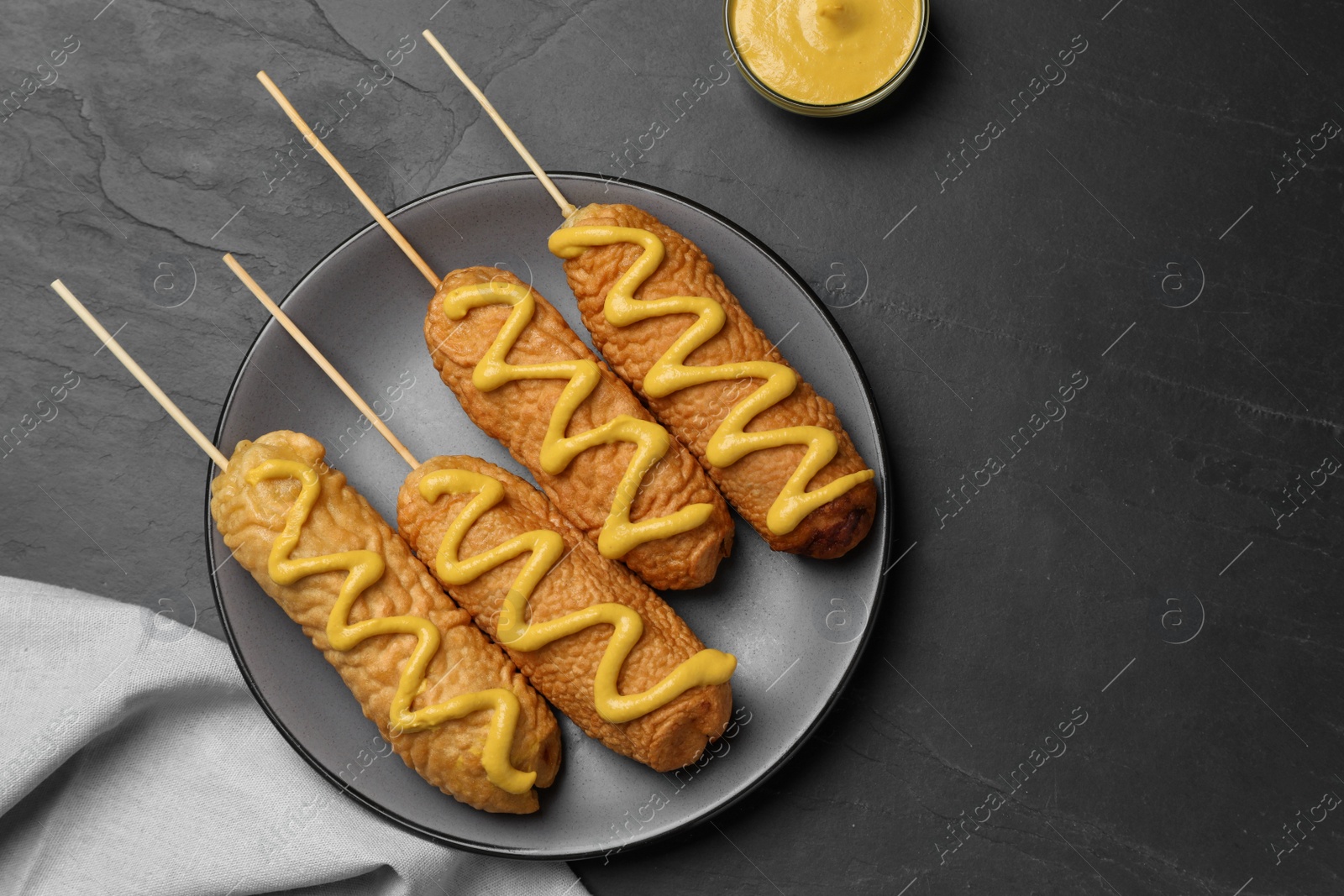 Photo of Delicious deep fried corn dogs with mustard on black table, top view