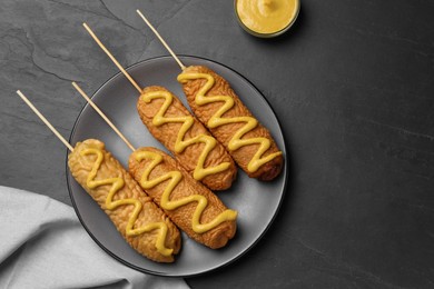 Photo of Delicious deep fried corn dogs with mustard on black table, top view