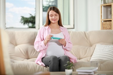 Photo of Beautiful pregnant woman holding box with pills at home