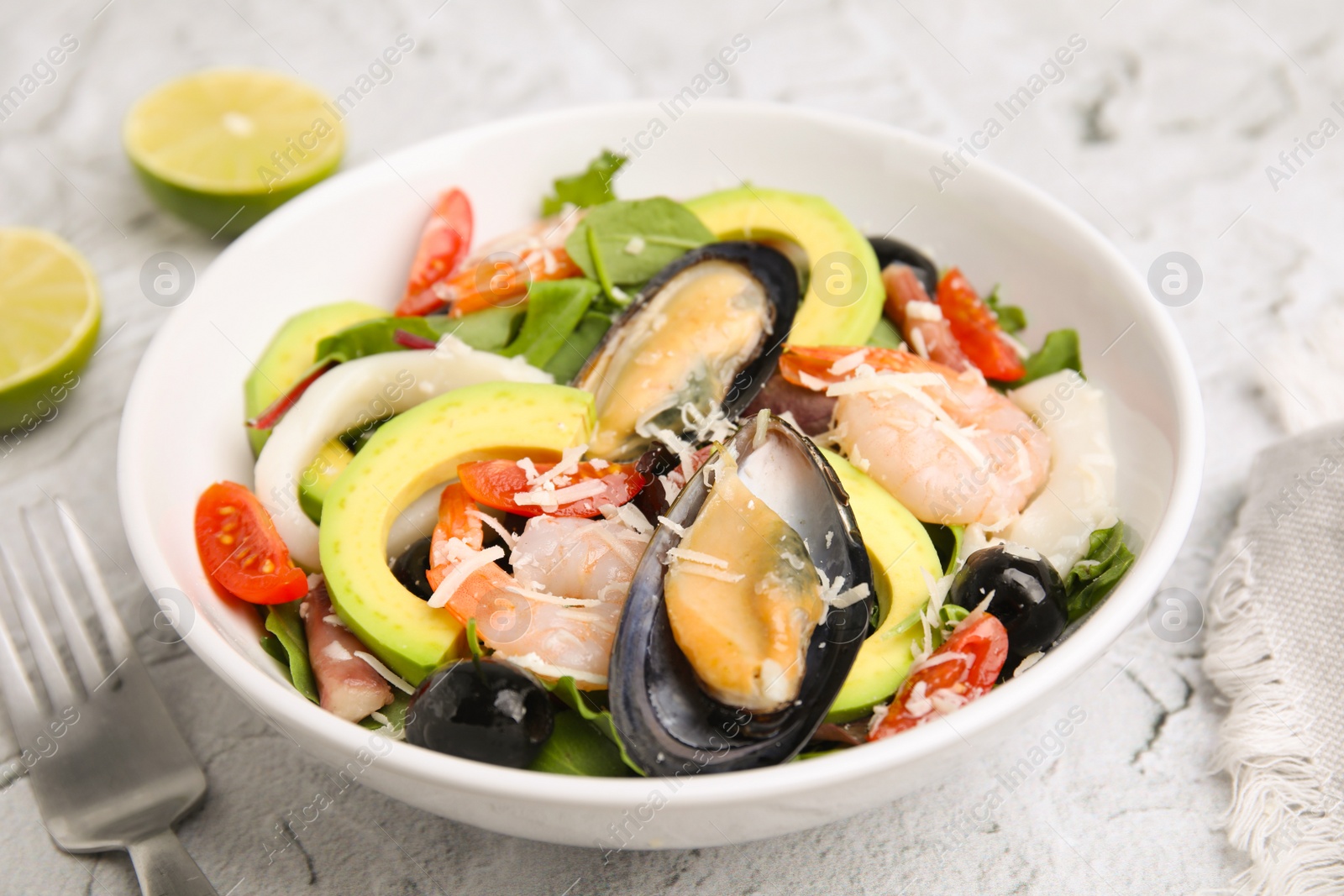 Photo of Bowl of delicious salad with seafood on white textured table, closeup