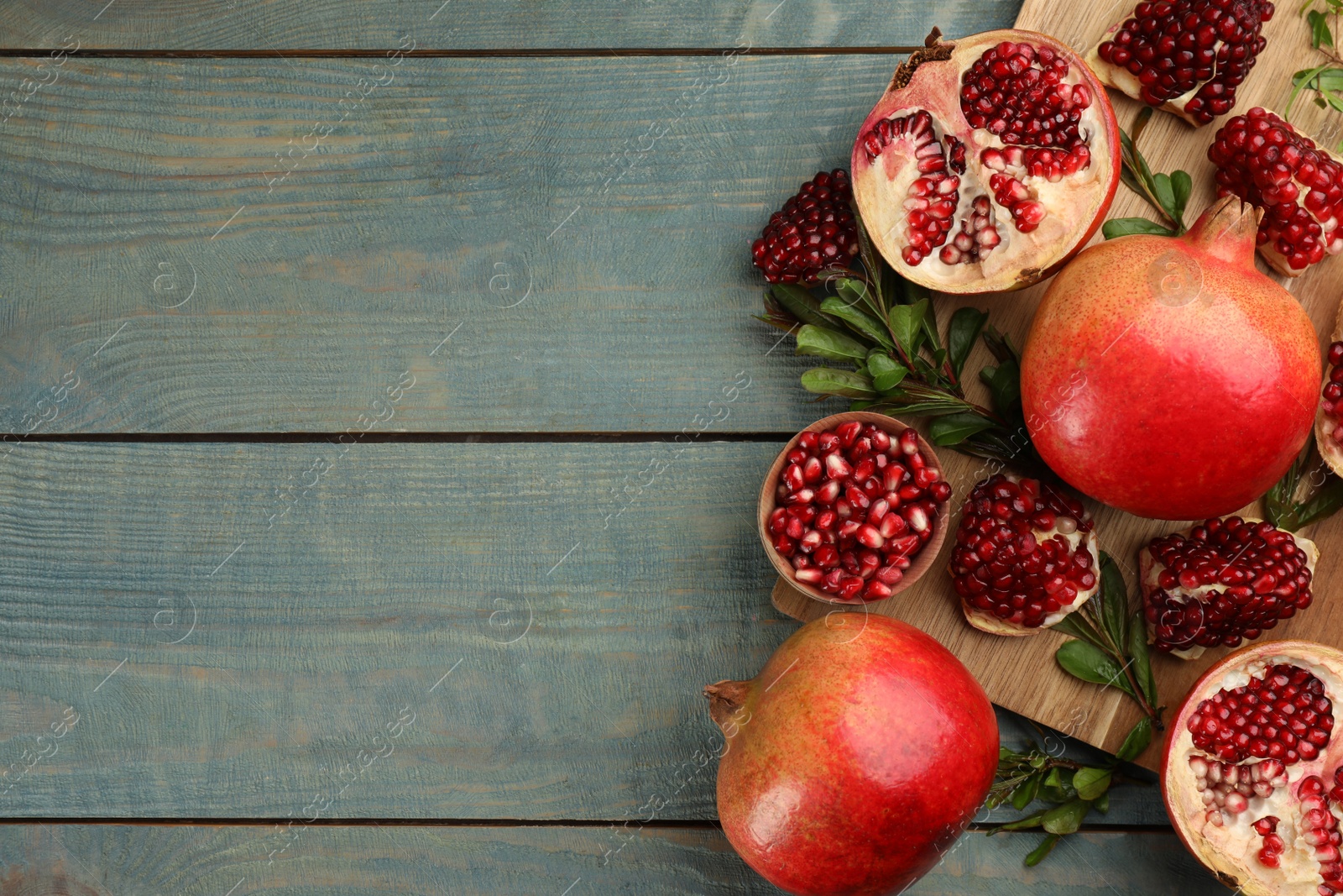 Photo of Delicious ripe pomegranates on blue wooden table, flat lay. Space for text