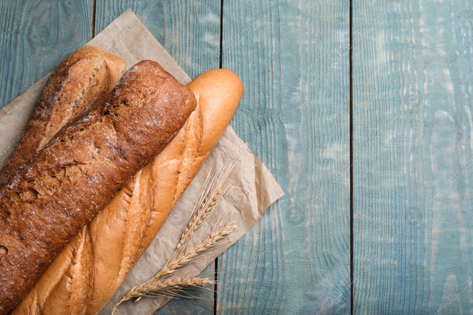 Photo of Different tasty baguettes on light blue wooden table, flat lay. Space for text