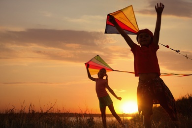 Photo of Cute little children playing with kites outdoors at sunset. Spending time in nature