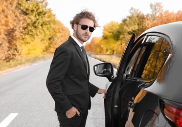 Young businessman opening car door on sunny day, outdoors