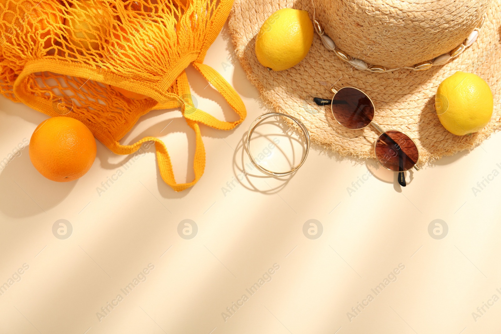 Photo of String bag with sunglasses, fruits and summer accessories on beige background, flat lay. Space for text