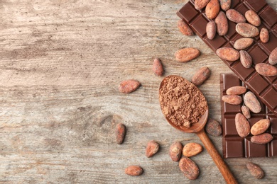 Flat lay composition with cocoa powder, beans and chocolate bar on wooden background