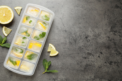 Photo of Ice cubes with lemon and mint in tray on grey table, flat lay. Space for text