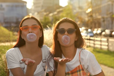 Beautiful women in sunglasses blowing gums outdoors