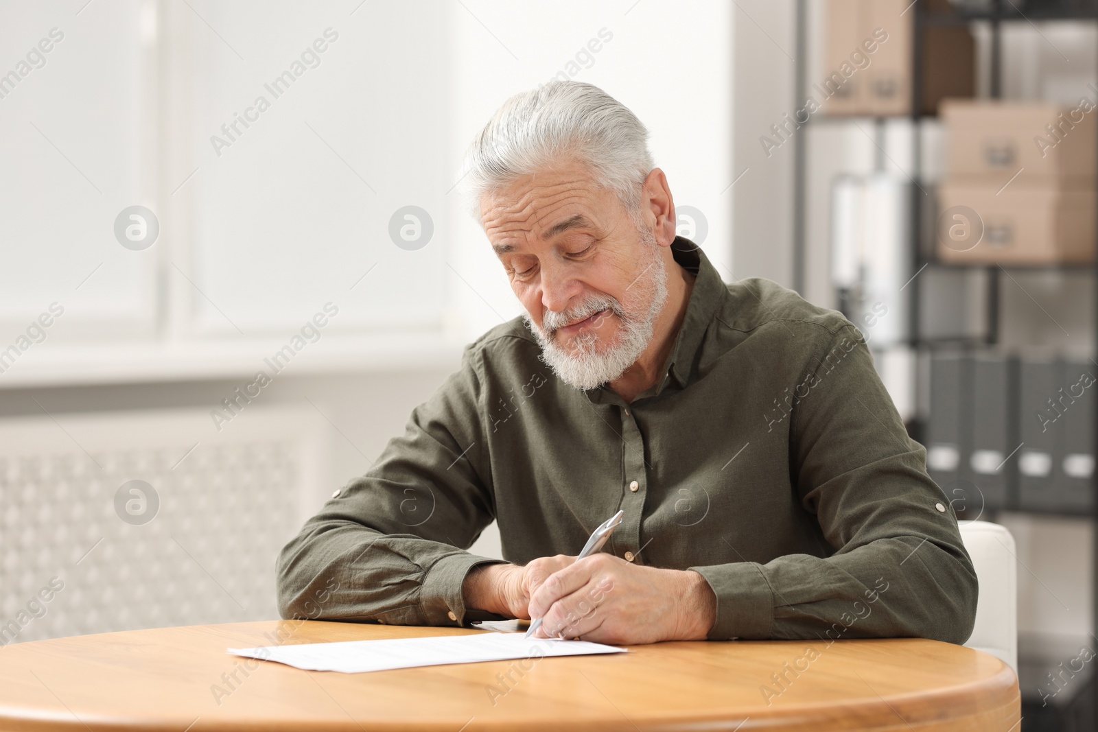 Photo of Senior man signing Last Will and Testament at table indoors. Space for text