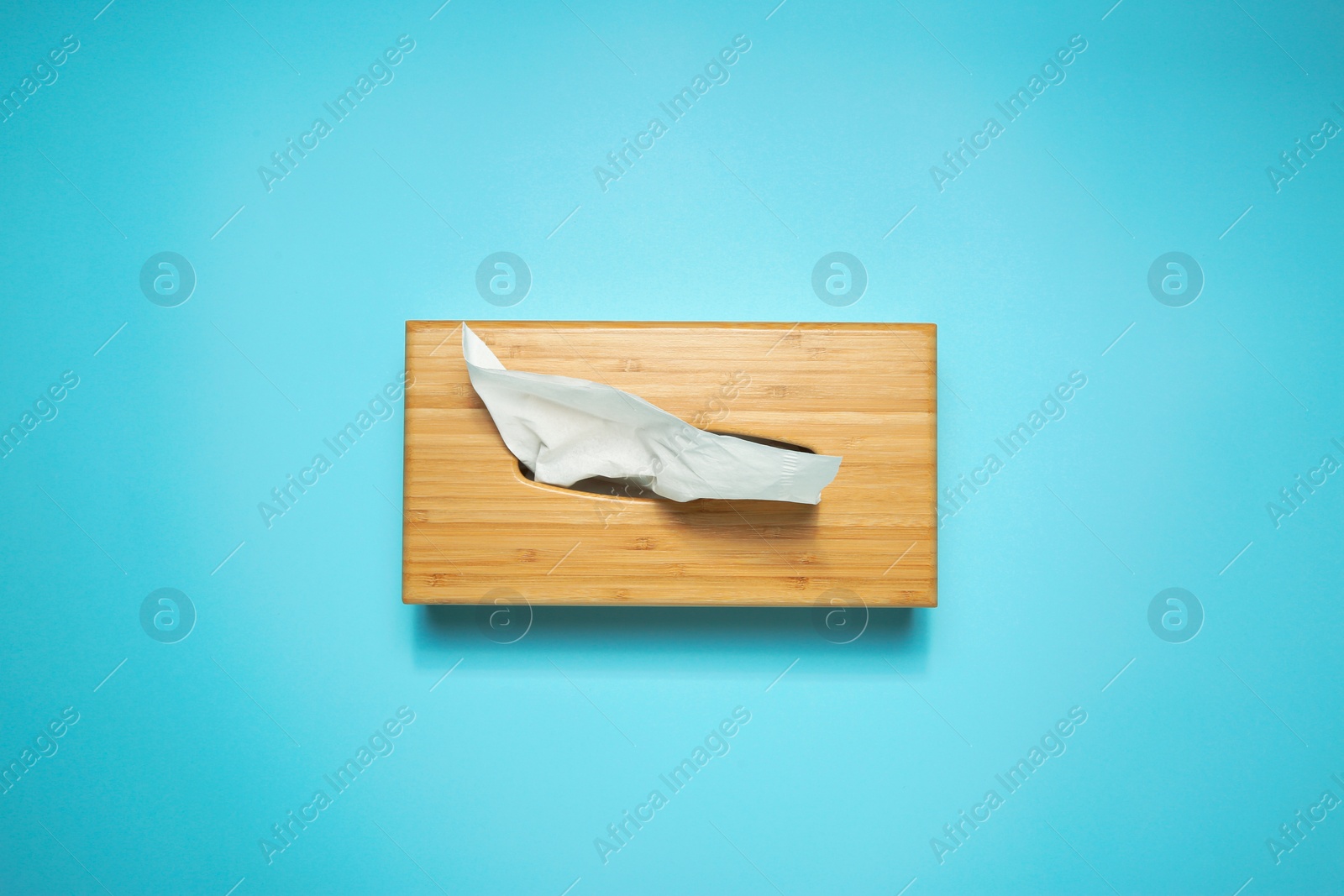 Photo of Wooden holder with paper tissues on light blue background, top view