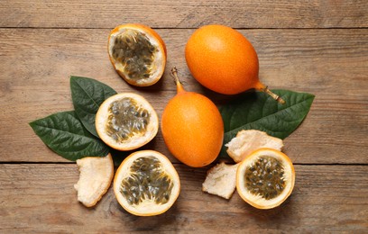 Photo of Delicious ripe granadillas and leaves on wooden table, flat lay