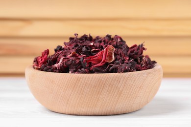 Dry hibiscus tea in bowl on white table, closeup