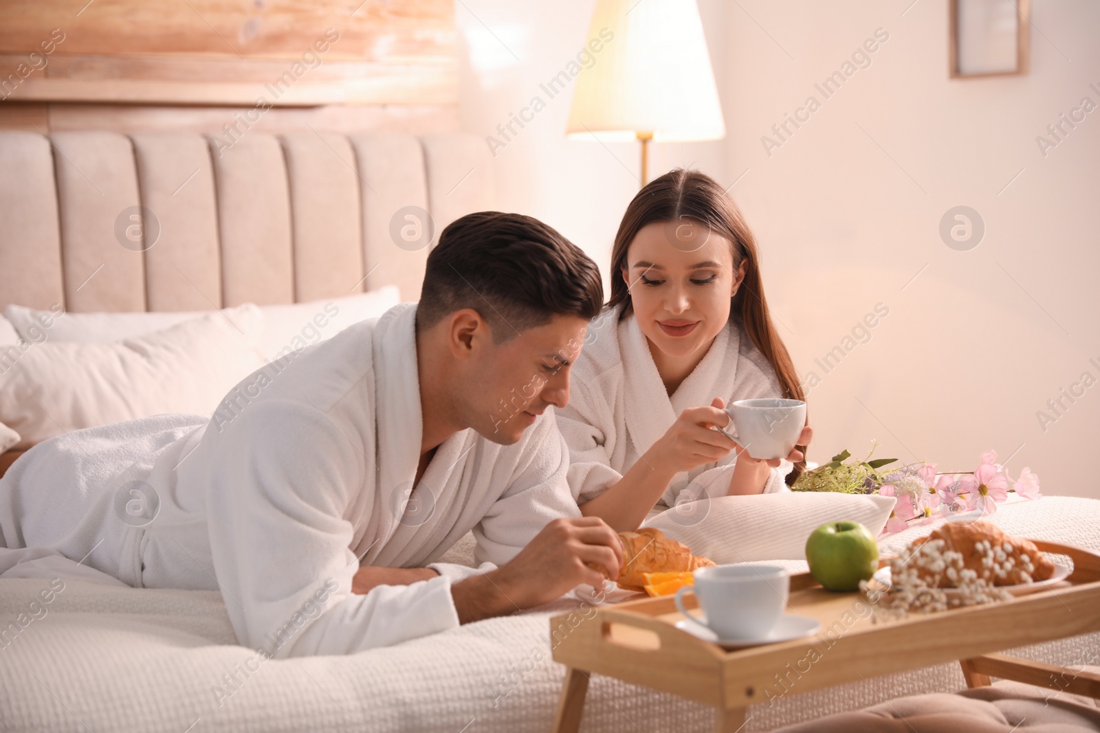 Photo of Happy couple in bathrobes having breakfast on bed at home