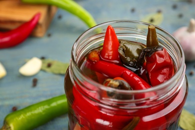 Photo of Glass jar of pickled chili peppers on light blue table, closeup
