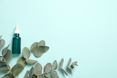 Photo of Aromatherapy product. Bottle of essential oil and eucalyptus branches on light blue background, flat lay. Space for text