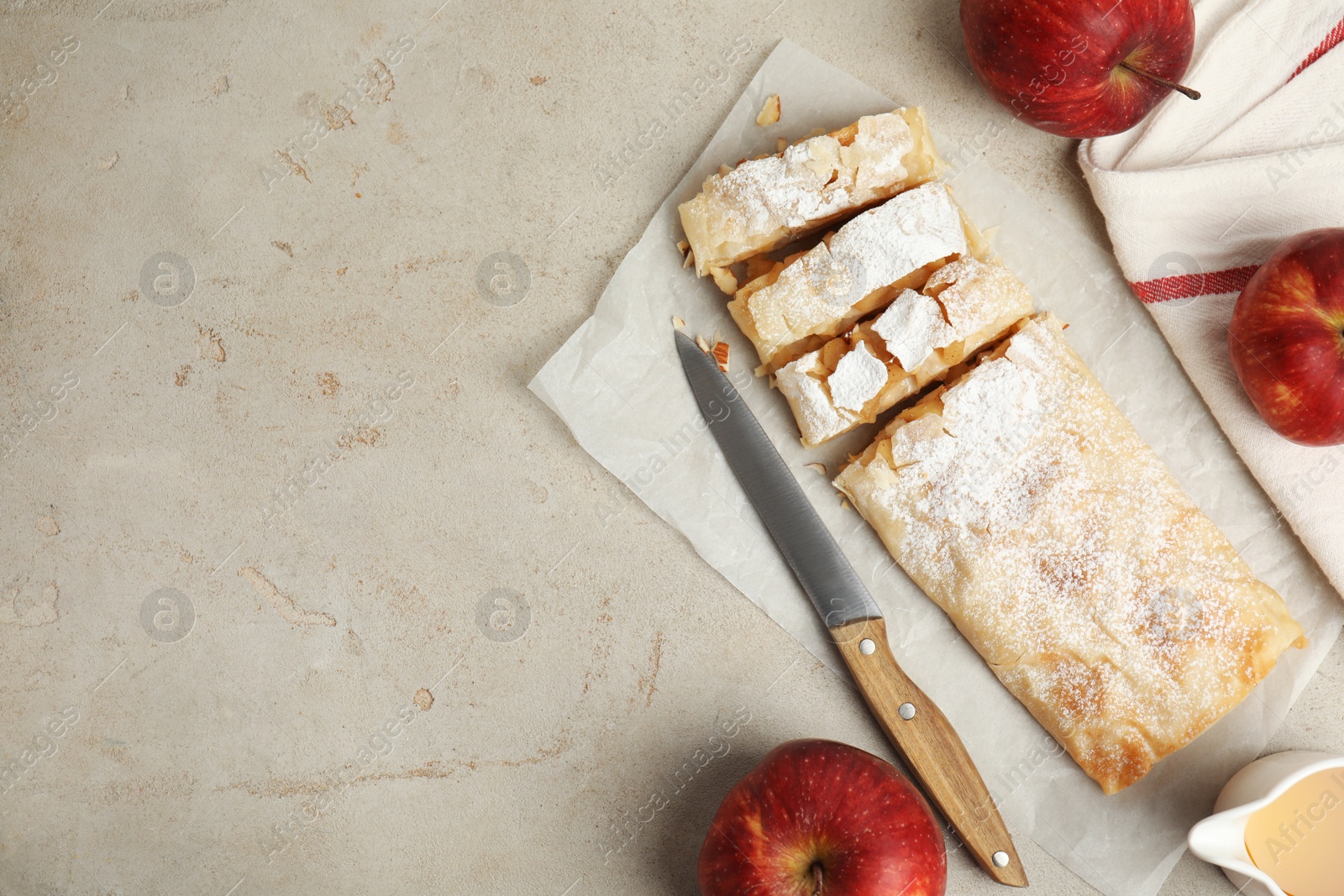 Photo of Delicious strudel, knife and fresh apples on light grey table, flat lay. Space for text