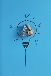 Photo of Composition with crumpled banknote and drawing of lamp bulb on color background, top view. Creative concept