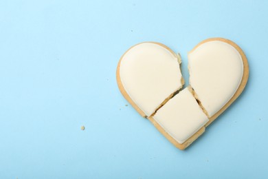 Photo of Broken heart shaped cookie on light blue background, top view with space for text. Relationship problems concept
