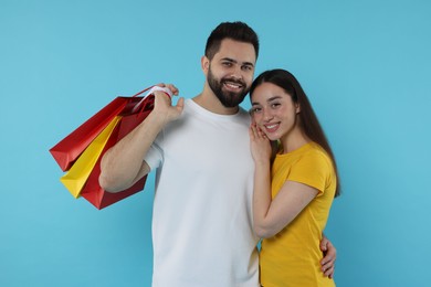 Photo of Happy couple with shopping bags on light blue background