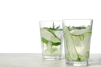 Glasses of refreshing cucumber lemonade and rosemary on wooden table against white background. Summer drink