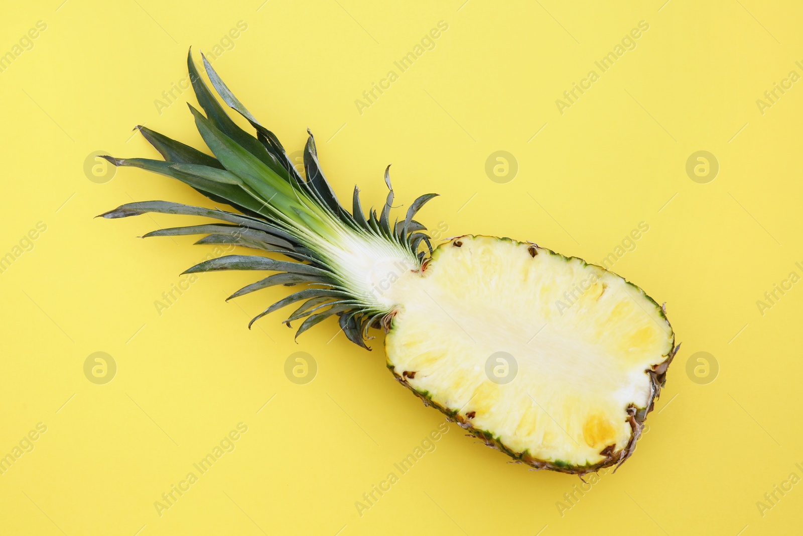 Photo of Half of ripe pineapple on yellow background, top view